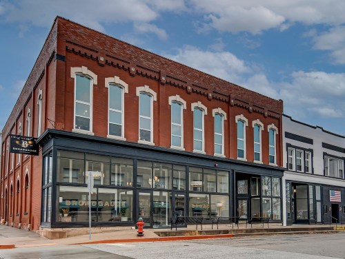Historic red brick building with large windows, featuring a sign for "Broadway" and a nearby American flag.