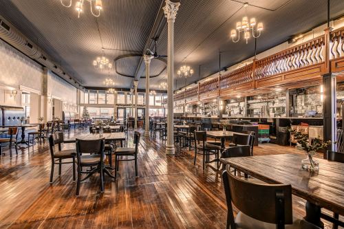 A spacious restaurant interior with wooden floors, elegant lighting, and a mix of tables and chairs.