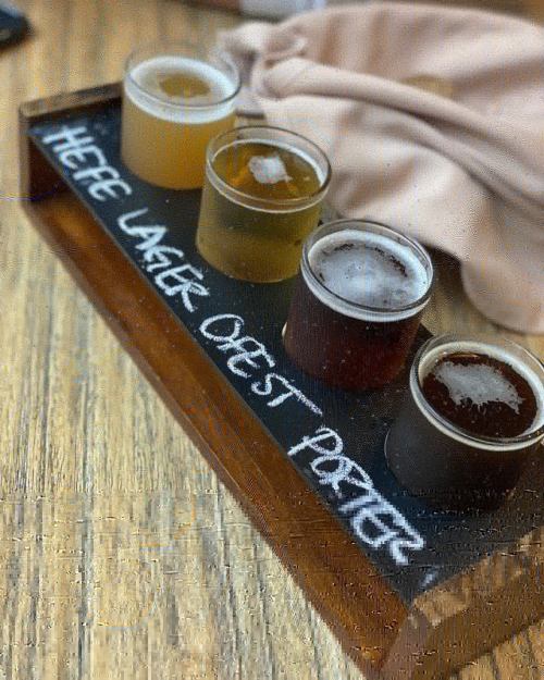 A wooden flight board with four small glasses of different beers, labeled "Three Lager, One Porter."