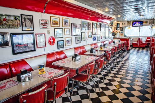 A retro diner interior with red booths, checkered floor, and walls adorned with vintage photos and memorabilia.