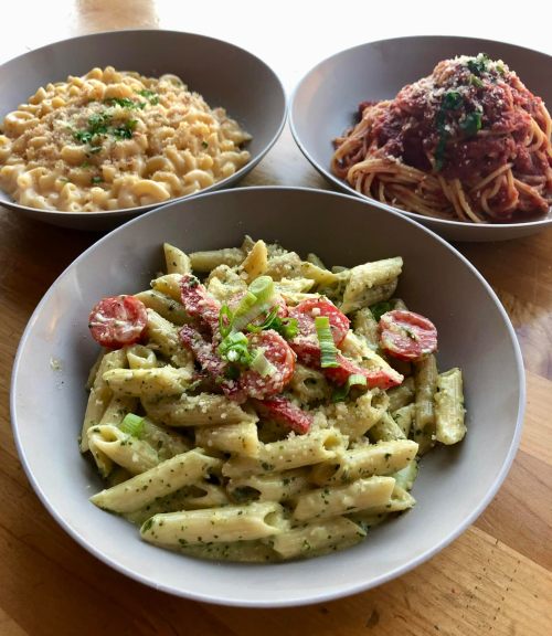 Three bowls of pasta: creamy mac and cheese, spaghetti with marinara, and penne with pesto and cherry tomatoes.