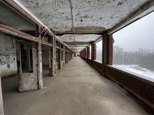 Abandoned corridor with weathered walls and large windows, overlooking a snowy landscape.