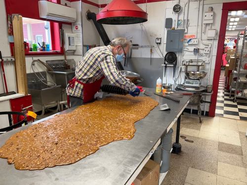 A person in an apron spreads a large batch of candy on a stainless steel table in a kitchen.