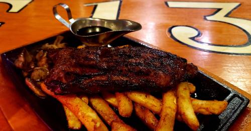 A sizzling plate of steak served with golden fries and a small gravy boat on a wooden table.