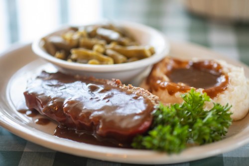 A plate featuring meatloaf with gravy, mashed potatoes, green beans, and a garnish of parsley.