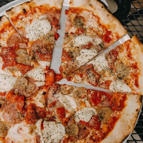 A freshly baked pizza with toppings of pepperoni, sausage, mozzarella, and herbs, sliced into eight pieces.