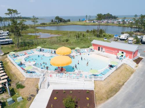 Aerial view of a vibrant pool area with a large yellow umbrella, surrounded by greenery and RVs in the background.