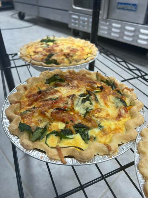 Two freshly baked quiches with spinach and cheese in silver pie tins, cooling on a wire rack.