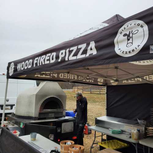 A food vendor tent with a wood-fired pizza oven and a person preparing food outdoors.