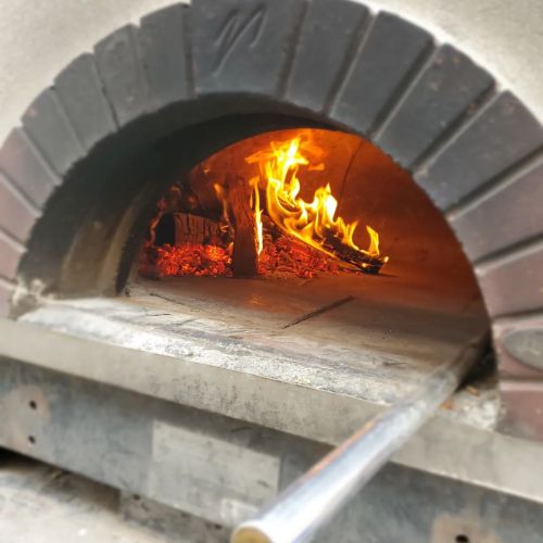 A close-up of a wood-fired oven with flames and glowing embers inside, ready for cooking.
