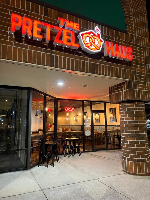 Exterior view of "The Pretzel Haus" with illuminated signage and an open sign, featuring a modern seating area.