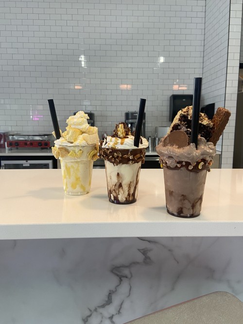 Three colorful milkshakes topped with whipped cream and various toppings, displayed on a marble counter.