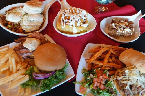 A spread of delicious dishes including biscuits, burgers, fries, sweet potatoes, and desserts on a red tablecloth.