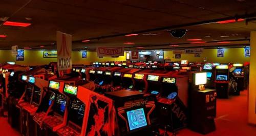 A vibrant arcade filled with classic gaming machines, illuminated by colorful lights and retro signage.