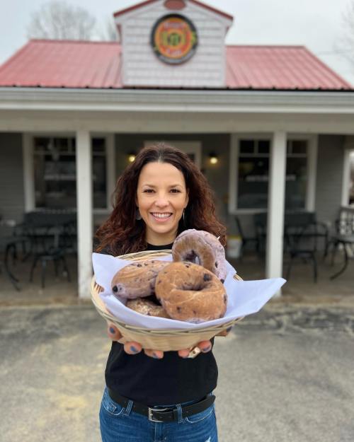 A woman holds a basket of donuts in front of a quaint shop with a red roof.