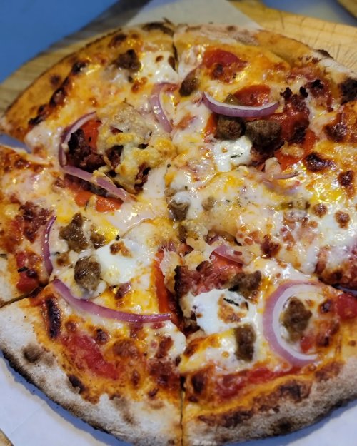 A freshly baked pizza topped with cheese, pepperoni, sausage, tomatoes, and red onions on a golden crust.