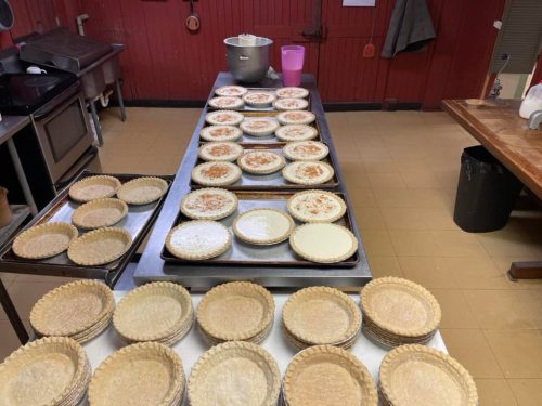 A kitchen counter filled with unbaked pie crusts arranged on trays, ready for filling.