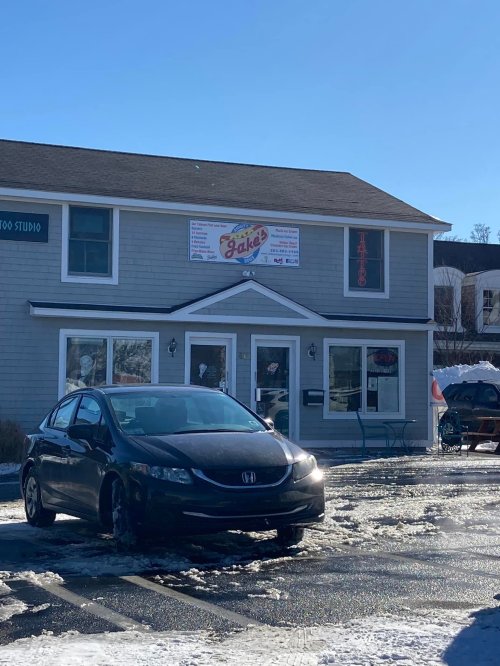 A black car parked in front of a two-story building with a sign for "Jake's" and snow on the ground.