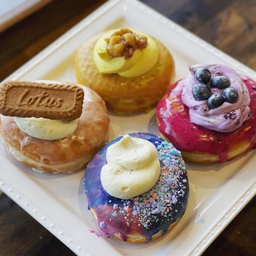 A plate of four colorful donuts topped with cream, fruit, and a Lotus cookie, showcasing vibrant glazes and decorations.