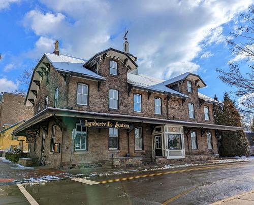 Historic stone building with a sign reading "Lambertville Station," set against a cloudy sky. Snow on the ground.