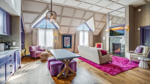 Cozy living room with modern decor, featuring a fireplace, colorful furniture, and large windows.