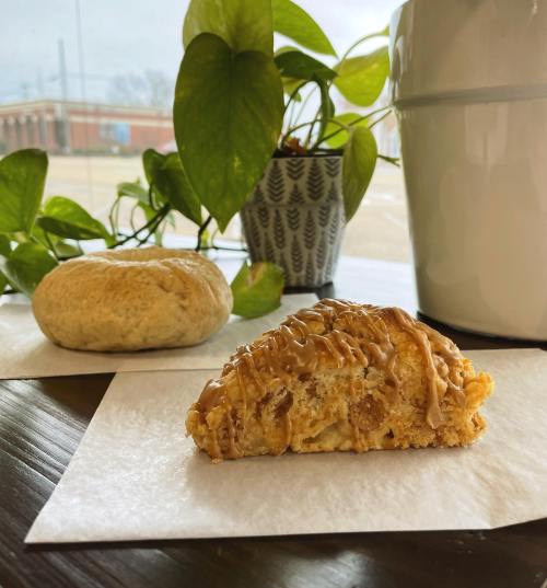 A close-up of two baked goods on white paper, with a potted plant in the background and a sunny outdoor view.