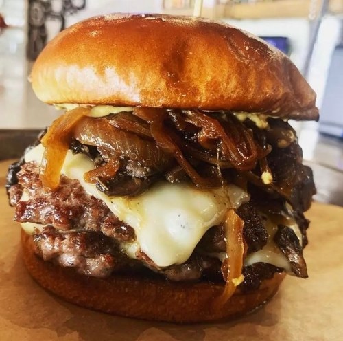 A juicy burger with melted cheese, caramelized onions, and a glossy bun, served on a paper-lined plate.