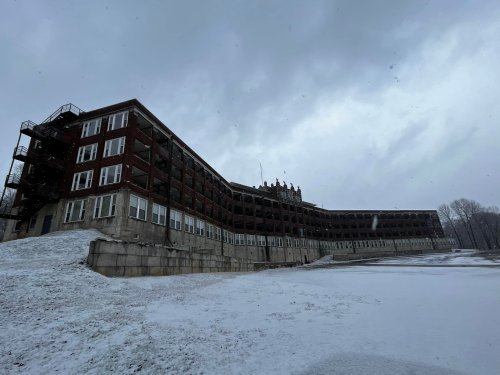 Abandoned building with multiple stories, snow-covered ground, and a cloudy sky.