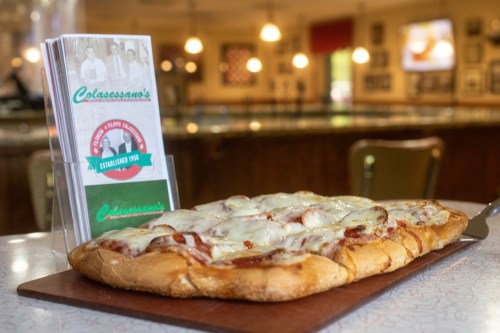 A freshly baked pizza with melted cheese and toppings, served on a wooden board next to a menu in a restaurant.