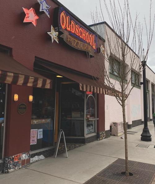 Exterior of Oldschool Pizzeria with colorful star signage and a tree in front, on a city street.