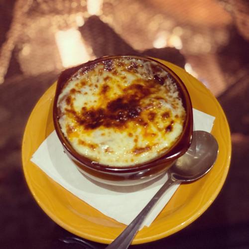 A bowl of creamy, baked dish with a golden, crispy top, served on an orange plate with a spoon beside it.