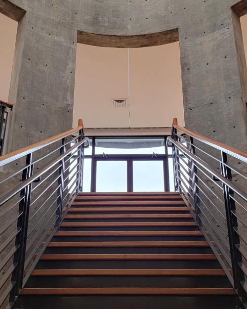 A modern staircase with wooden steps and metal railings, leading up to large windows and natural light.