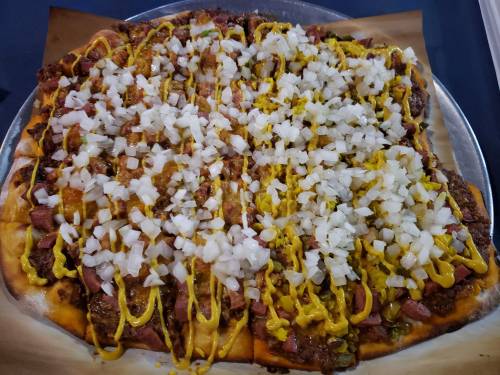 A large square pizza topped with diced onions and yellow mustard, featuring a mix of meats on one half.