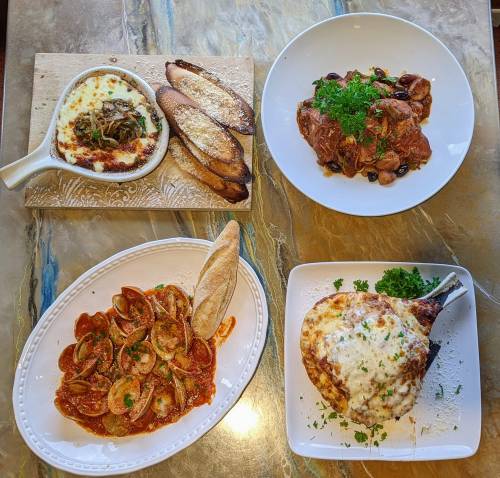 A spread of Italian dishes: baked cheese, pasta, meat with olives, and a cheesy chicken dish, all garnished with herbs.