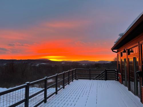 A vibrant sunset casts orange and pink hues over a snowy landscape, viewed from a wooden deck.