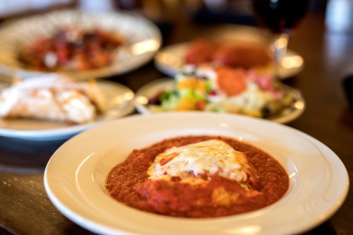 A plate of enchiladas topped with cheese and red sauce, surrounded by various other dishes in the background.