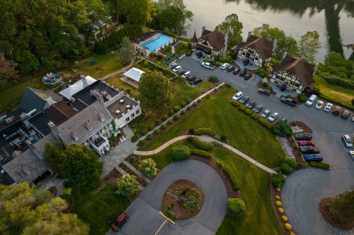 Aerial view of a large estate with a pool, landscaped gardens, and a parking area filled with cars.