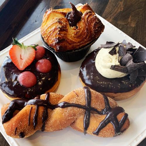 A plate of assorted pastries: a croissant, chocolate-covered donuts with fruit, and a twisted chocolate drizzled pastry.
