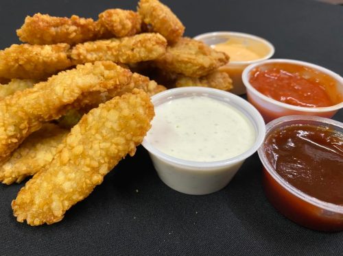 Crispy golden chicken strips with three dipping sauces: ranch, barbecue, and marinara, on a black background.