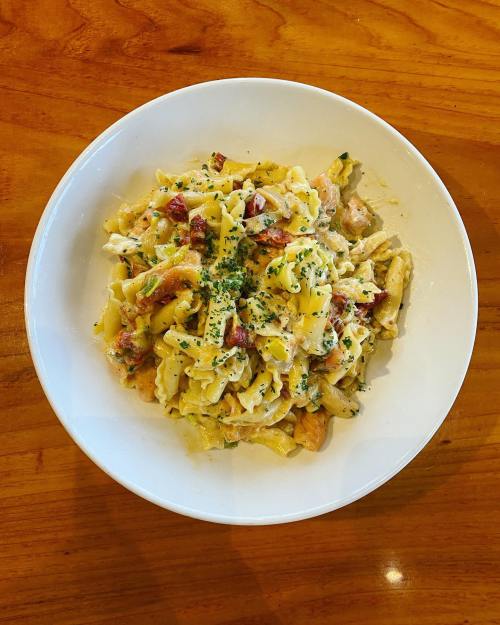 A bowl of creamy pasta with chicken, herbs, and a light sauce, served on a wooden table.