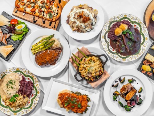 A variety of gourmet dishes displayed on white tablecloth, including meats, vegetables, and sauces.