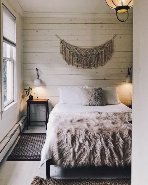 Cozy bedroom with a white bed, fur throw, macramé wall art, and warm lighting from bedside lamps.