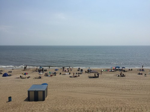 A sunny beach scene with people lounging on the sand, colorful umbrellas, and gentle waves in the background.