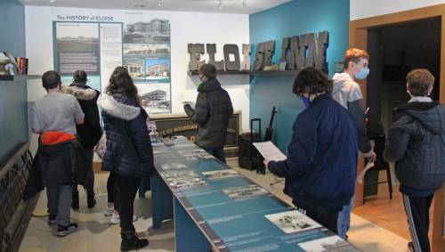 Visitors explore a museum exhibit about local history, examining displays and photographs while wearing masks.
