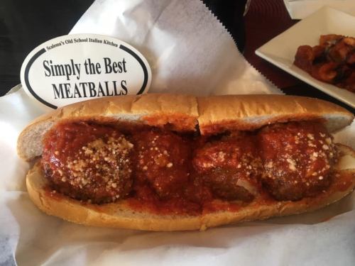 A sub sandwich filled with meatballs and marinara sauce, topped with cheese, served with a sign that says "Simply the Best MEATBALLS."