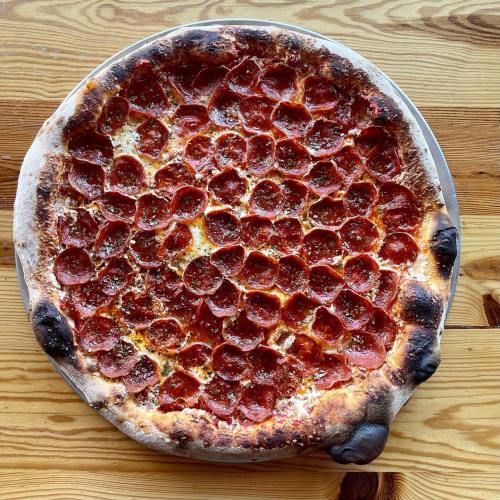 A large pepperoni pizza with a crispy crust, topped generously with slices of pepperoni and herbs, on a wooden table.