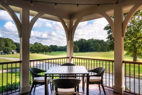 A cozy outdoor patio with a table and chairs, overlooking a green landscape and cloudy sky.