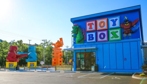 Colorful toy store exterior with large playful sculptures of robots and dinosaurs outside, bright blue building.