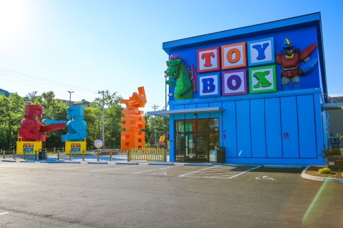 Colorful toy store exterior featuring large toy sculptures and a bright blue building with "TOY BOX" signage.