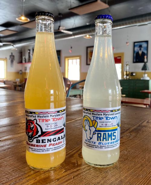Two bottles of flavored lemonade on a wooden table: one labeled "Bengals Cranberry Peach" and the other "Rams White Blueberry."